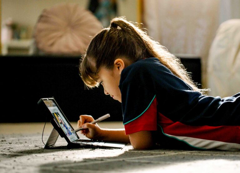 a virtual learning distance ed school student lays on the floor writing on a tablet